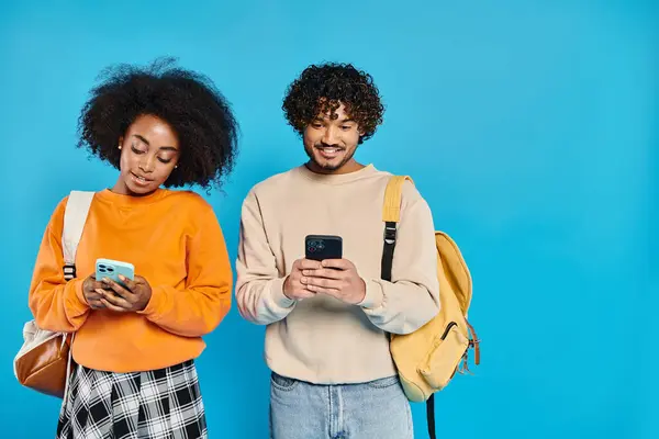 Una pareja multicultural de estudiantes de pie junto a teléfonos inteligentes en un estudio, mostrando unidad y amistad. - foto de stock