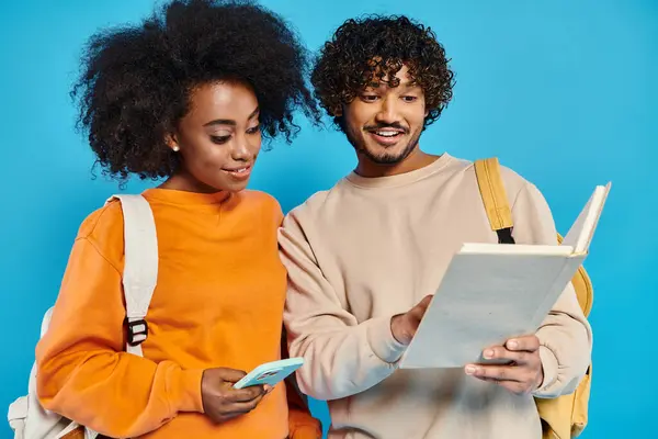 An interracial man and woman standing, examining a piece of paper together in a studio setting on a blue backdrop. — Stock Photo