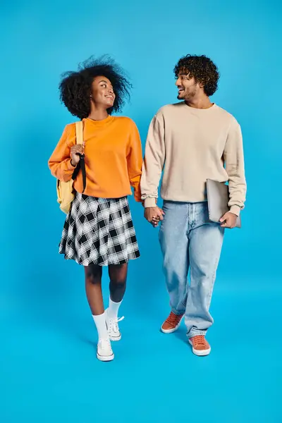 An interracial couple, casually dressed, takes a leisurely walk together against a vibrant blue backdrop in a studio setting. — Stock Photo