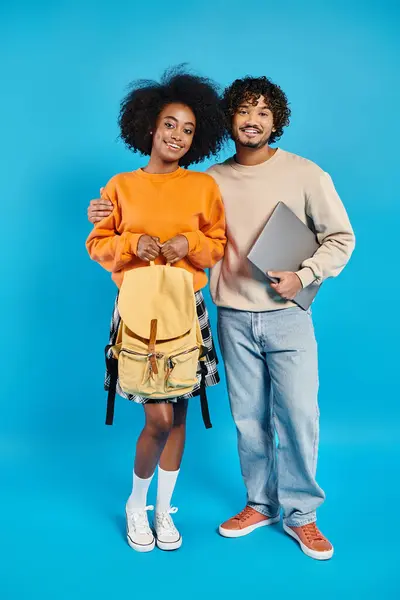 Um casal inter-racial de estudantes estão juntos em traje casual contra um pano de fundo azul em um estúdio. — Fotografia de Stock