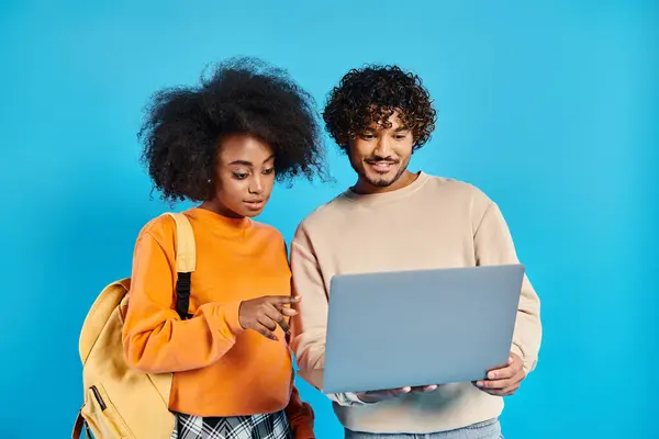 Um casal inter-racial de estudantes estão juntos, absorvidos em uma tela de laptop, compartilhando um momento de colaboração e descoberta. — Fotografia de Stock