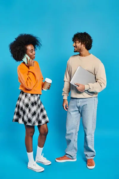 Un homme et une femme, étudiants interraciaux, se tiennent côte à côte en tenue décontractée sur fond bleu. — Photo de stock
