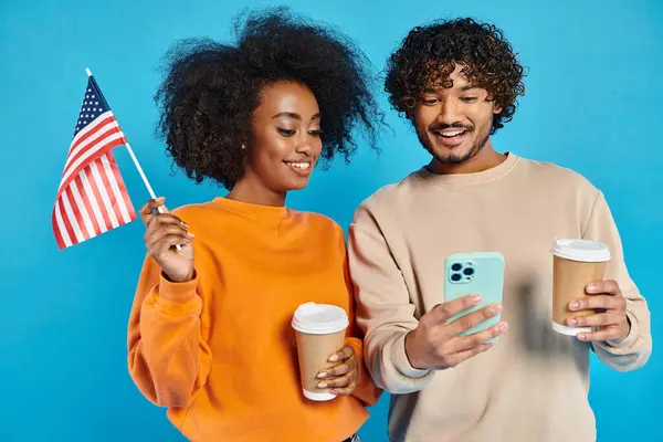 Una pareja interracial se para sosteniendo una taza de café y un teléfono celular, disfrutando de un momento de conexión. - foto de stock