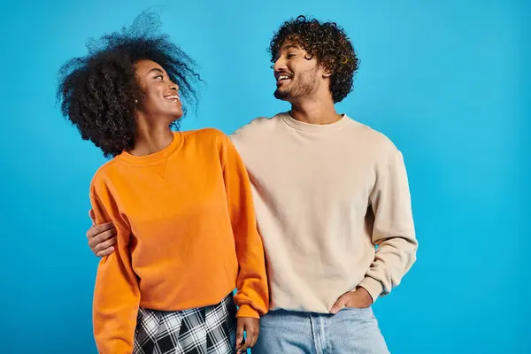 An African-American woman and indian man, both students, stand together in casual attire against a blue backdrop. — Stock Photo