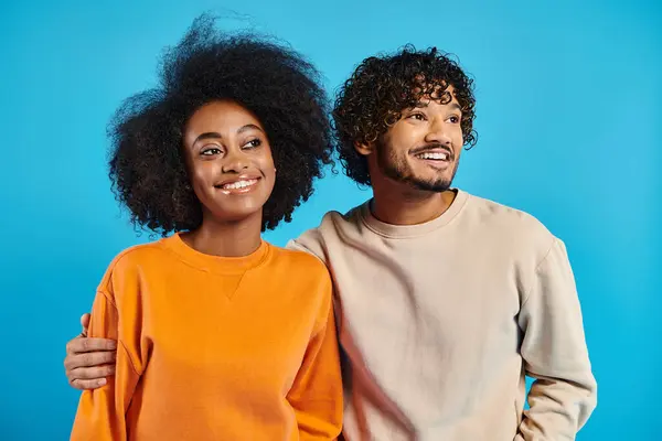 A man and a woman, interracial students, strike a pose in casual attire against a blue backdrop in a studio. — Stock Photo
