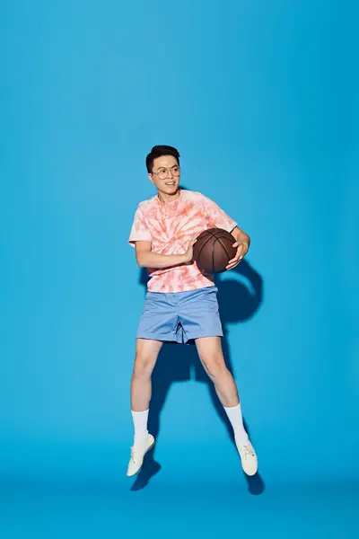 Un giovane uomo elegante posa con una pallacanestro su uno sfondo blu vibrante, trasudando fiducia e atletismo. — Foto stock