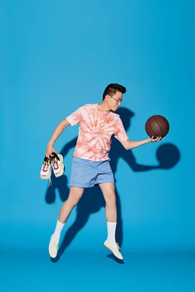 A trendy young man striking a pose with a basketball in front of a vibrant blue background. — Stock Photo
