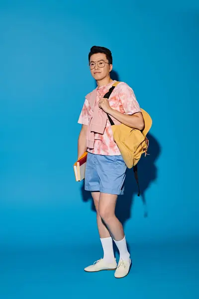 Uomo elegante in camicia rosa e pantaloncini blu con una borsa gialla, in posa energica su uno sfondo blu. — Foto stock