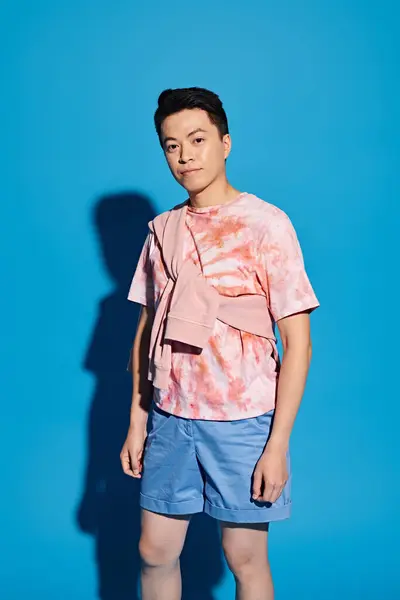Ein stilvoller junger Mann in trendiger Kleidung posiert vor einer leuchtend blauen Wand und strahlt Zuversicht und Charme aus. — Stockfoto