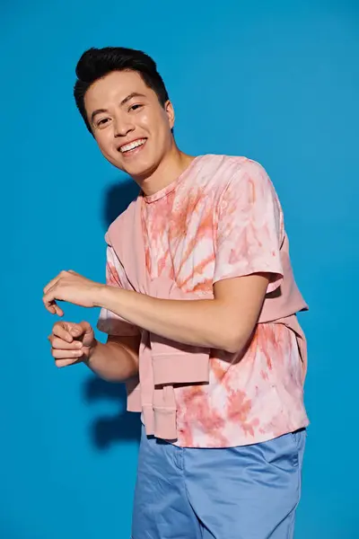 Elegante joven posando enérgicamente en una camisa rosa y pantalones azules sobre un vibrante telón de fondo azul. - foto de stock