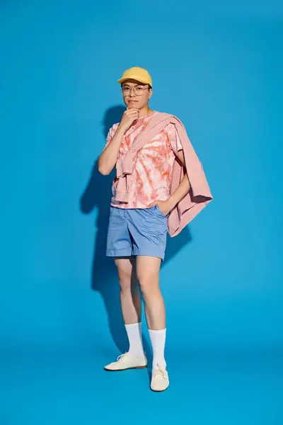 Un joven elegante y guapo posa activamente en un atuendo de moda sobre un vibrante telón de fondo azul. - foto de stock