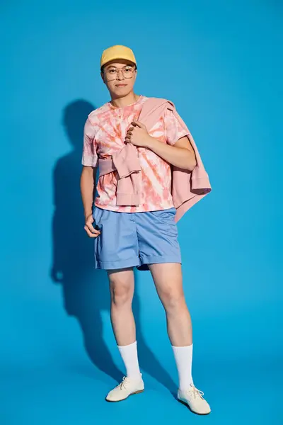 Молодой человек, стильно одетый в розовую рубашку и синие шорты, энергично позирует на синем фоне. — стоковое фото