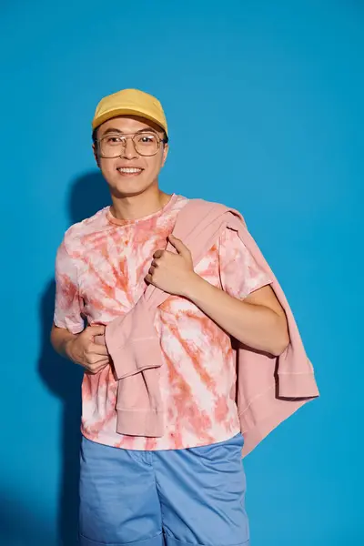 Stylish young man posing energetically in a trendy pink shirt and blue shorts against a vibrant blue backdrop. — Stock Photo