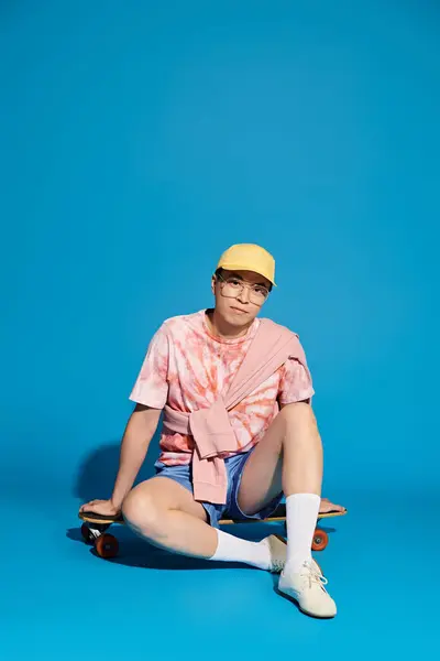 Un giovane elegante in abiti alla moda si siede a terra con uno skateboard, abbracciando un momento di relax. — Foto stock