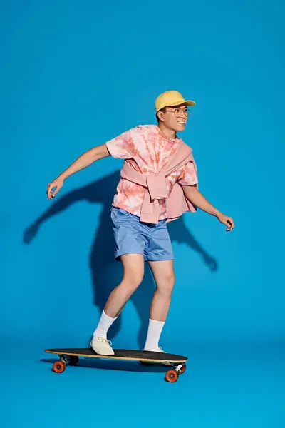 Ein stylischer, gut aussehender junger Mann in trendiger Kleidung skatet aktiv auf einem lebendigen blauen Hintergrund. — Stockfoto