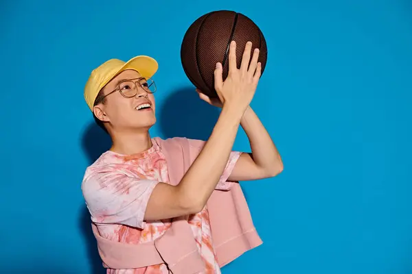 A stylish woman in a yellow hat confidently holds a basketball, exuding energy and strength against a vibrant backdrop. — Stock Photo
