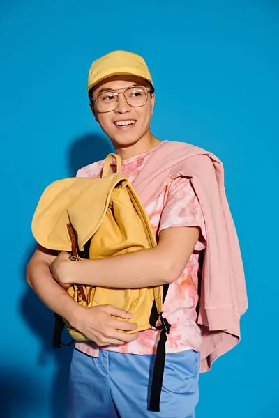 Молодой человек в розовой рубашке наносит модную позу на синем фоне в ярко-желтой шляпе. — стоковое фото
