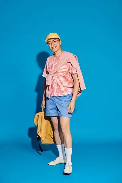 A stylish young man posing actively in trendy attire in front of a vibrant blue background. — Stock Photo
