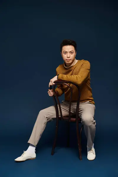 A fashionable young man, dressed in elegant attire, sits on top of a wooden chair in a dynamic pose. — Stock Photo