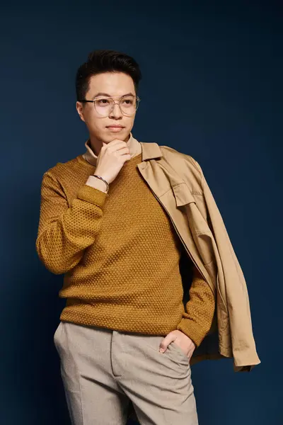 Un giovane alla moda in un maglione marrone e occhiali colpisce una posa riflessiva. — Foto stock
