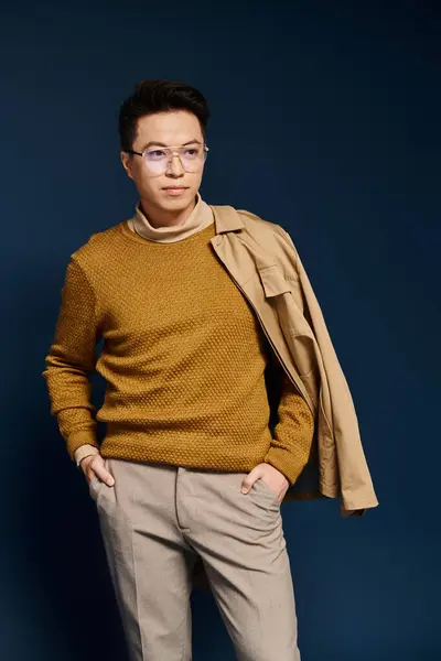 Un giovane elegante con occhiali e un maglione si erge con fiducia davanti a uno sfondo blu vibrante. — Foto stock