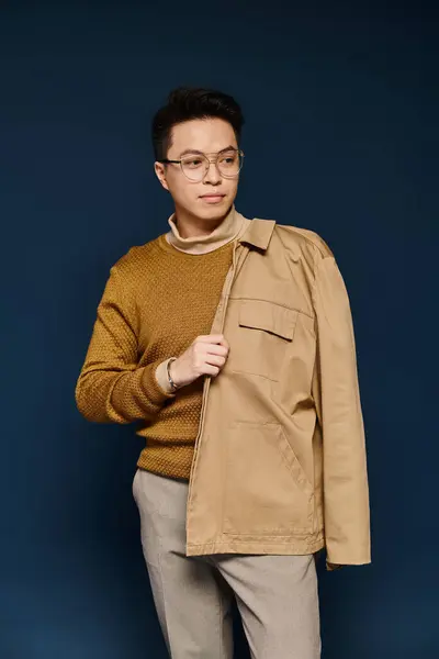 Un joven de moda posando activamente en un suéter marrón y pantalones bronceados. - foto de stock
