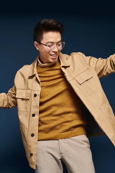 Un joven de moda en gafas y una chaqueta bronceada alcanza una pose, exudando confianza y sofisticación. - foto de stock