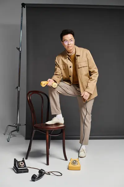 Un hombre de moda con un atuendo elegante se sienta con confianza en la parte superior de una silla al lado de un teléfono. - foto de stock