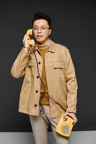 Модный молодой человек в коричневой куртке активно взаимодействует с желтым телефоном. — стоковое фото