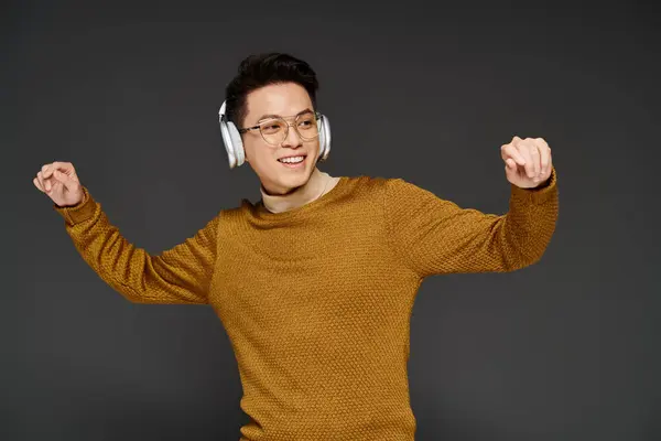 A fashionable young man energetically poses in a cozy sweater while wearing headphones, exuding a trendy and sophisticated vibe. — Stock Photo