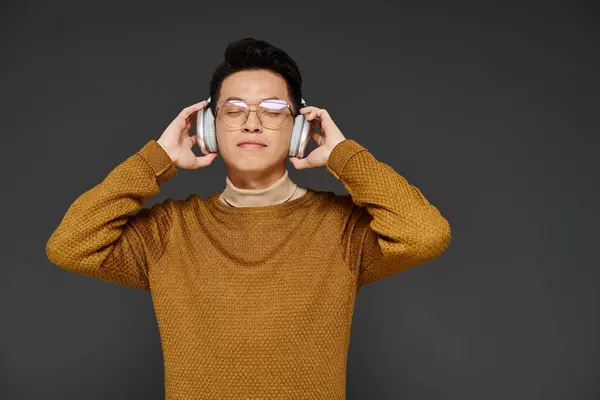Un joven con estilo y elegante atuendo escuchando atentamente a través de auriculares mientras usa gafas. - foto de stock