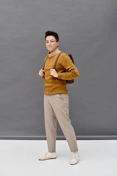 Um jovem na moda em uma camisola marrom e calças brancas golpeia uma pose dinâmica. — Fotografia de Stock