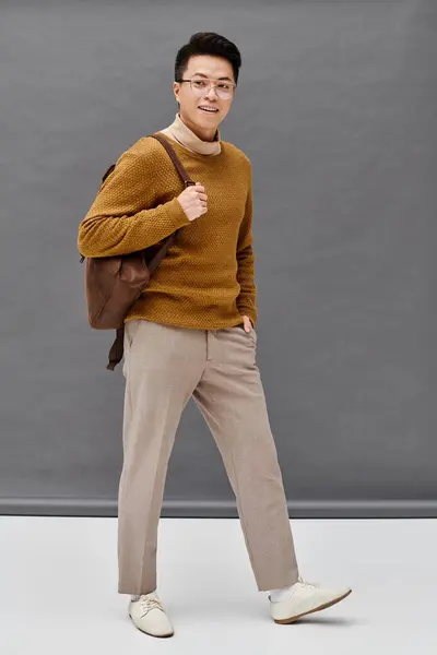 Модний молодий чоловік вражає динамічну позу в коричневому светрі і засмагах, демонструючи свій елегантний одяг. — стокове фото