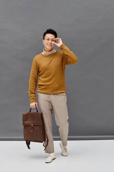 Un joven de moda con un atuendo elegante sosteniendo un maletín, exudando confianza y alegría mientras sonríe a la cámara. - foto de stock