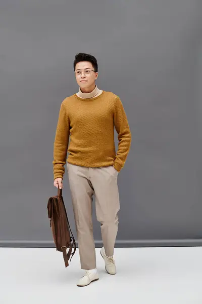 Un joven con estilo en un suéter marrón y pantalones blancos posa con confianza. - foto de stock