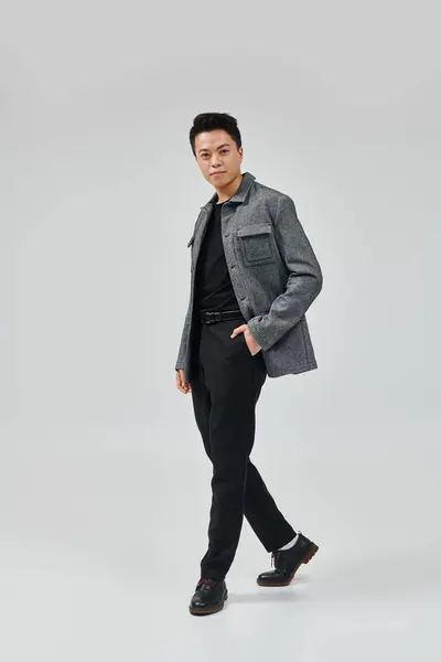 Ein modischer junger Mann posiert aktiv in grauer Jacke und schwarzer Hose und strahlt Eleganz und Stil aus. — Stockfoto