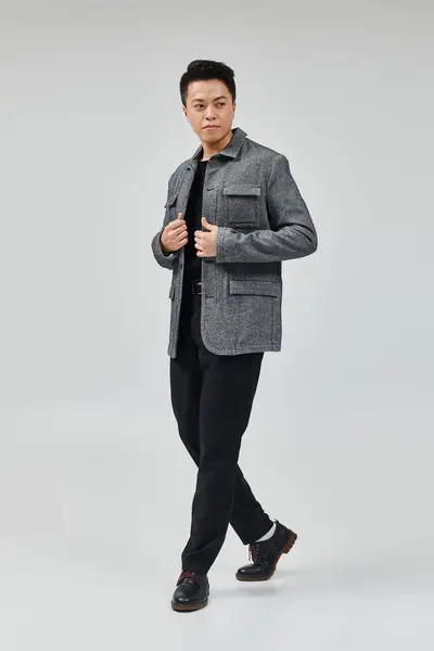 Un joven de moda con una chaqueta gris y pantalones negros golpeando una pose dinámica. - foto de stock