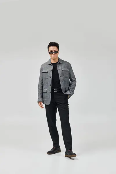 Un joven de moda posa activamente en una elegante chaqueta gris y pantalones negros. - foto de stock