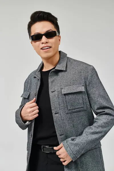 Модний молодий чоловік впевнено позує в пальто і сонцезахисні окуляри, виключаючи елегантність і витонченість. — стокове фото
