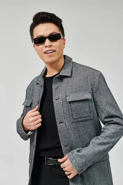 Un joven de moda posa con confianza en un abrigo y gafas de sol, exudando elegancia y sofisticación. — Stock Photo