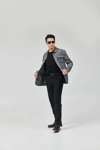 A fashionable young man strikes a dynamic pose in a gray jacket and black pants. — Stock Photo