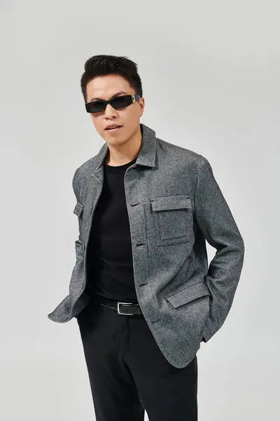 Un jeune homme à la mode respire la confiance dans une veste grise et un pantalon noir, posant de manière créative avec une énergie vibrante. — Photo de stock