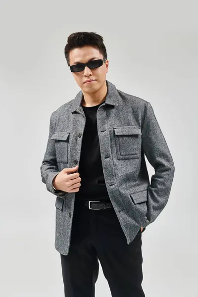 Un giovane alla moda colpisce una posa in un abito elegante, indossando occhiali da sole e una giacca. — Foto stock