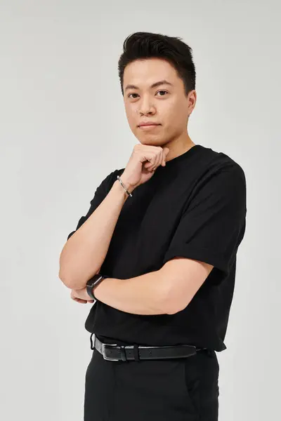 Un jeune homme à la mode en tenue élégante prend une pose confiante pour une caméra dans une chemise noire. — Photo de stock