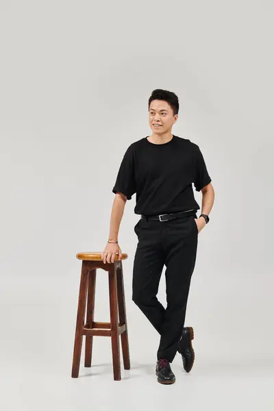 Модный молодой человек в элегантной одежде, ставящий позу возле деревянного стула. — стоковое фото