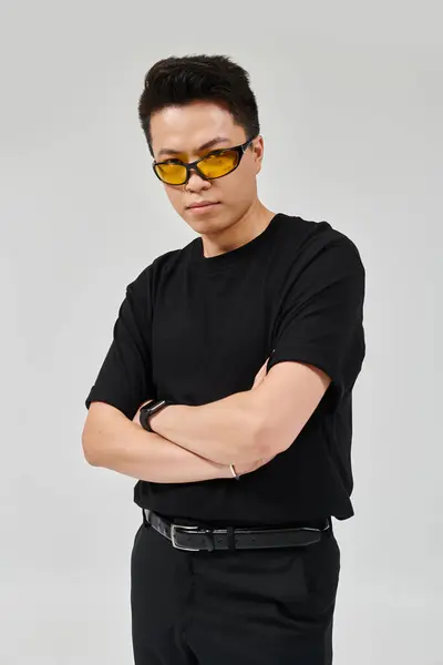 Un joven de moda con los brazos cruzados y gafas de sol golpea una pose segura con un atuendo elegante. - foto de stock