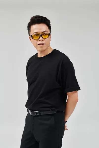 Ein modischer junger Mann posiert selbstbewusst in schwarzem Hemd und Sonnenbrille. — Stockfoto