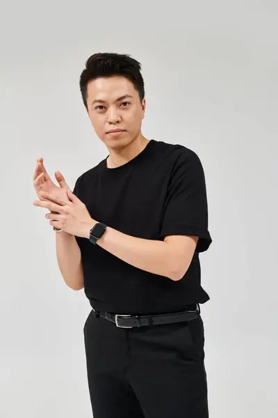Un jeune homme à la mode prend une pose confiante dans une chemise et un pantalon noirs, respirant élégance et style. — Photo de stock