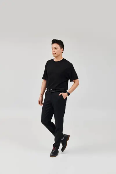 Un jeune homme à la mode pose en toute confiance dans un t-shirt et un pantalon noirs, respirant élégance et sophistication. — Photo de stock