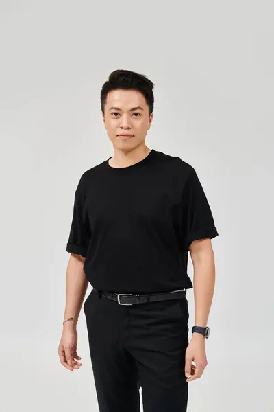 Модный молодой человек уверенно позирует в черной рубашке и брюках, источая элегантность и стиль. — стоковое фото